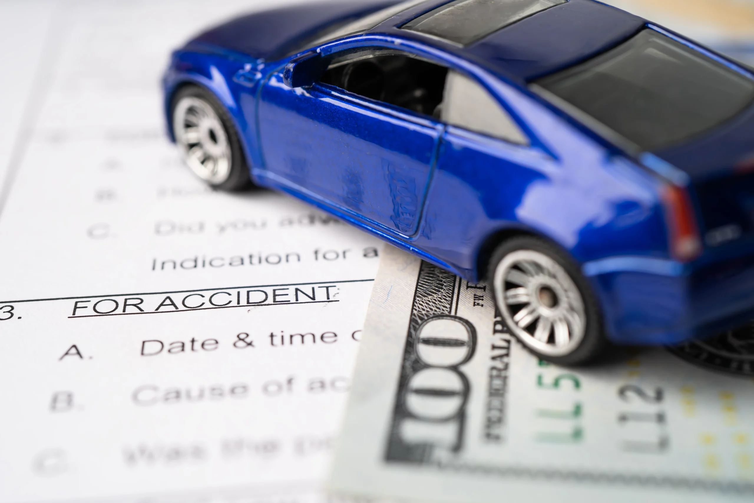 Toy car on top of hundred-dollar bills and accident paperwork, representing financial compensation, insurance claims, and legal deadlines related to New Jersey car accident cases and statute of limitations.
