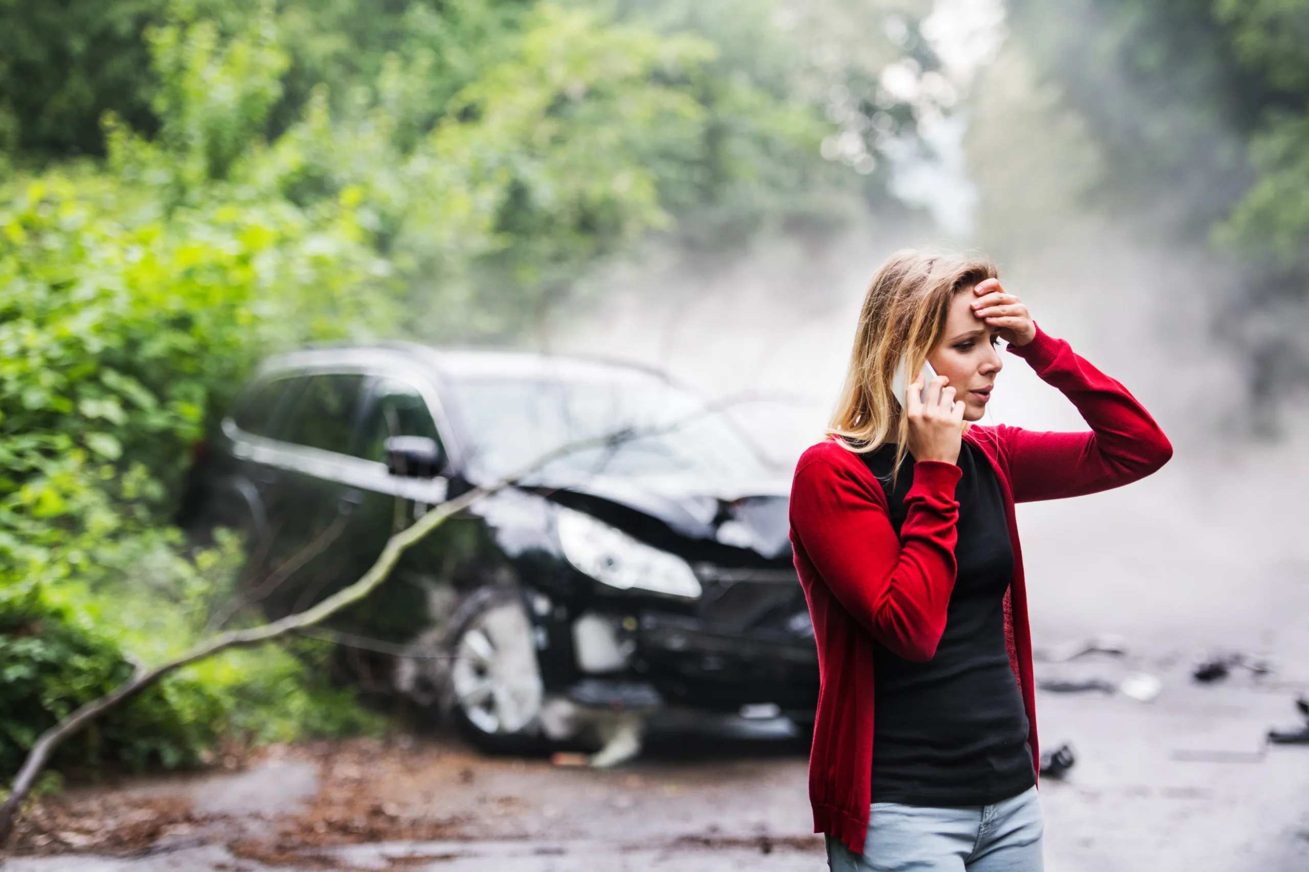 Distraught woman speaking on the phone beside a damaged car after a traffic accident on a foggy road, representing the important steps to take after a car accident in Clifton, New Jersey.