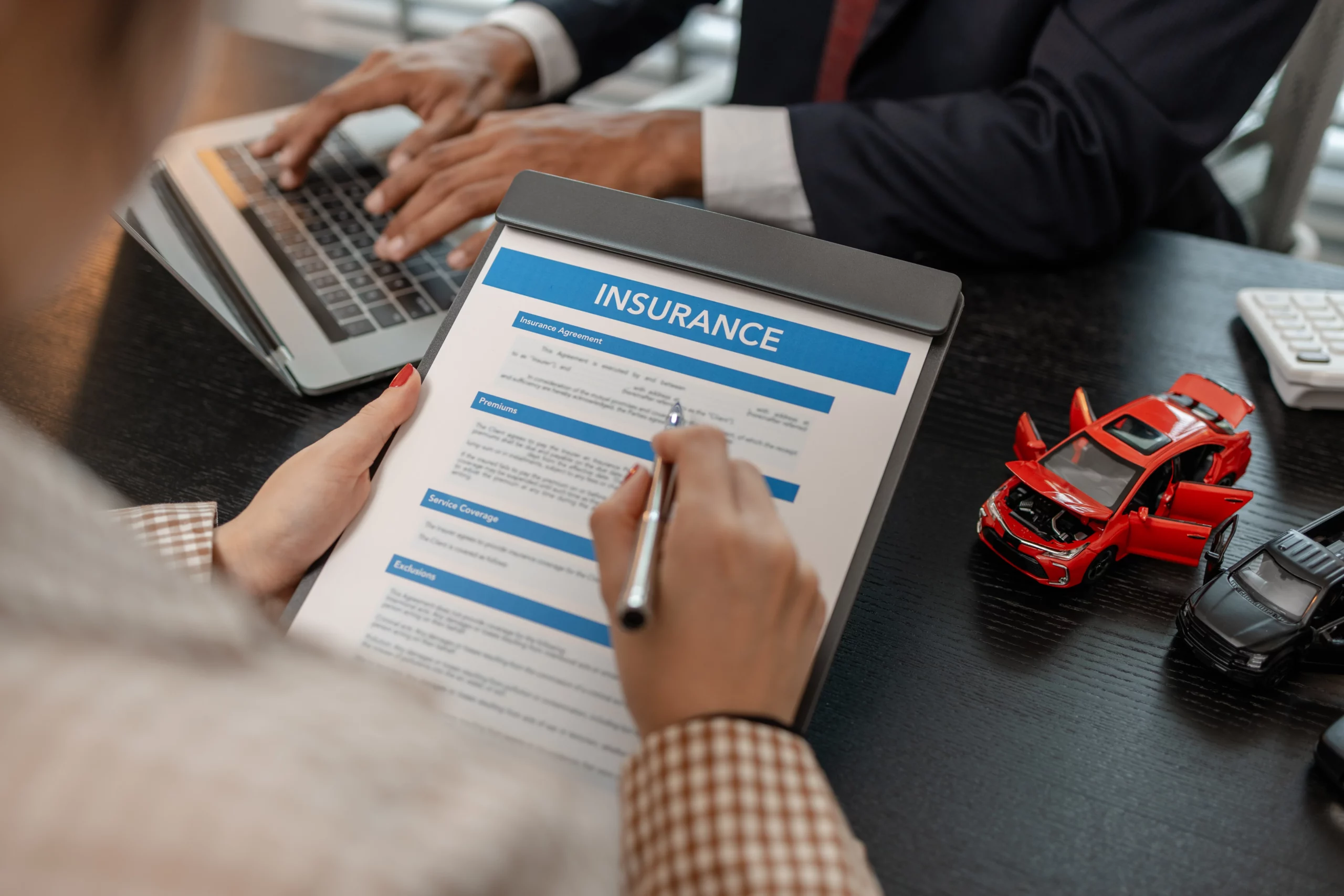 Person reviewing car insurance documents with toy vehicles and a calculator on the desk, representing verbal threshold laws and the right to sue after a New Jersey car accident.