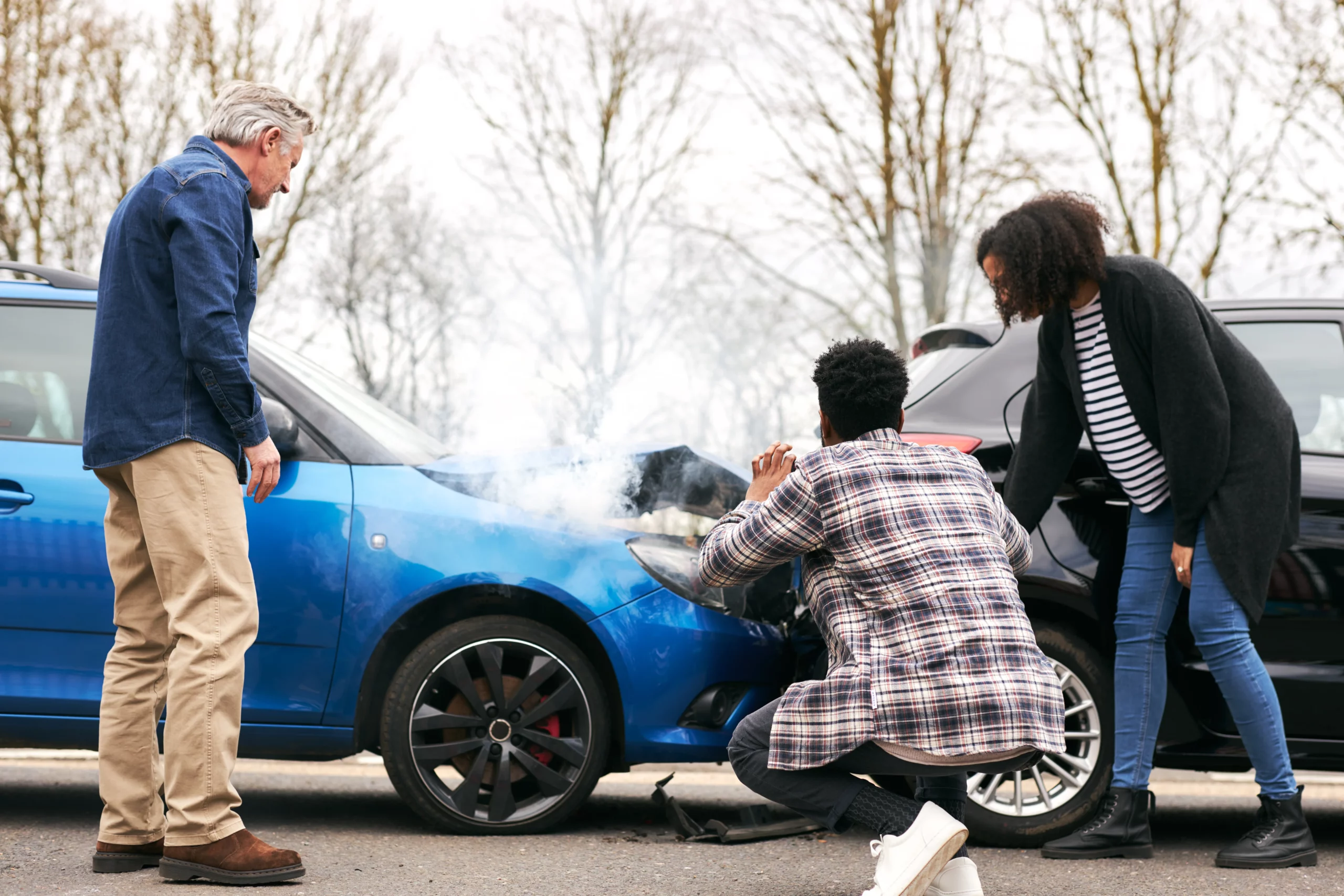 Drivers standing beside two damaged vehicles after a minor car accident, with smoke coming from one car’s engine, representing New Jersey no-fault insurance claims and accident liability laws.